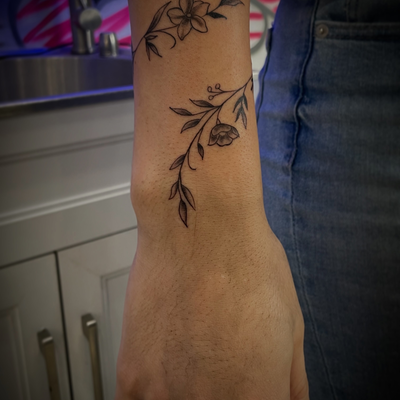 Cute wrap around vine with a few tiny flowers…her first tat ☺️ — tattoo by Jc TheArtist, Downey, California